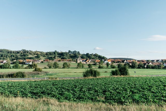 Neuhoff/Zenn, Panoramaaufnahme einer idyllischen Landschaft mit einem kleinem Ort mit Stadtmauer, viel Wiesen und Bäumen, Erlebnisort Neue Höfe 